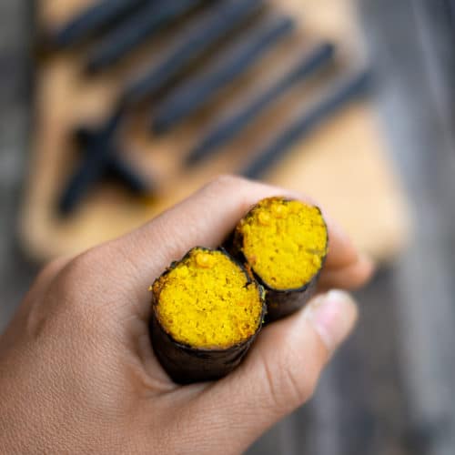 Hand Holding Nori Rolls with Turmeric Carrot and Nuts