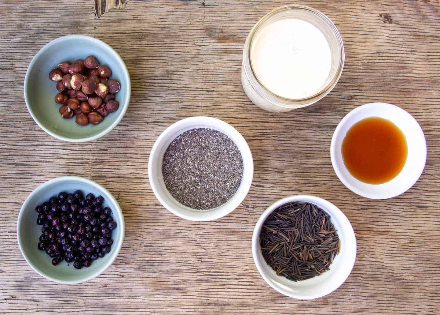Ingredients in Small Bowls: Chia seed, wild rice, milk alternative, hazelnuts, berries, maple syrup