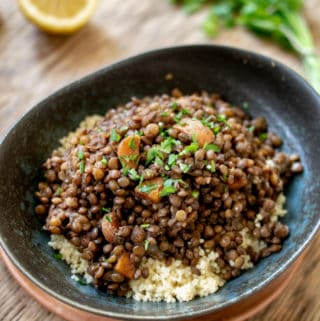 Close up of lentil stew on couscous with parsley and lemon in background