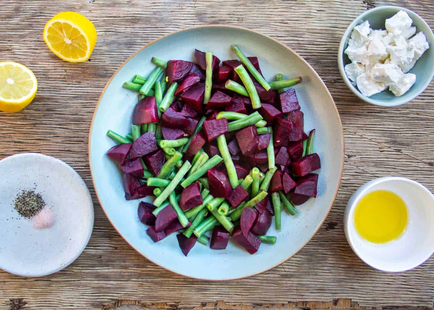Steamed beets and beans in blue bowl, with dressings on the side