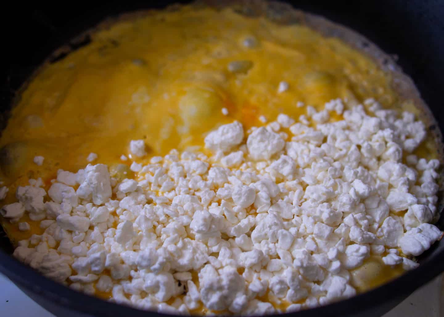 Dry cottage cheese on half of the eggs in frying pan
