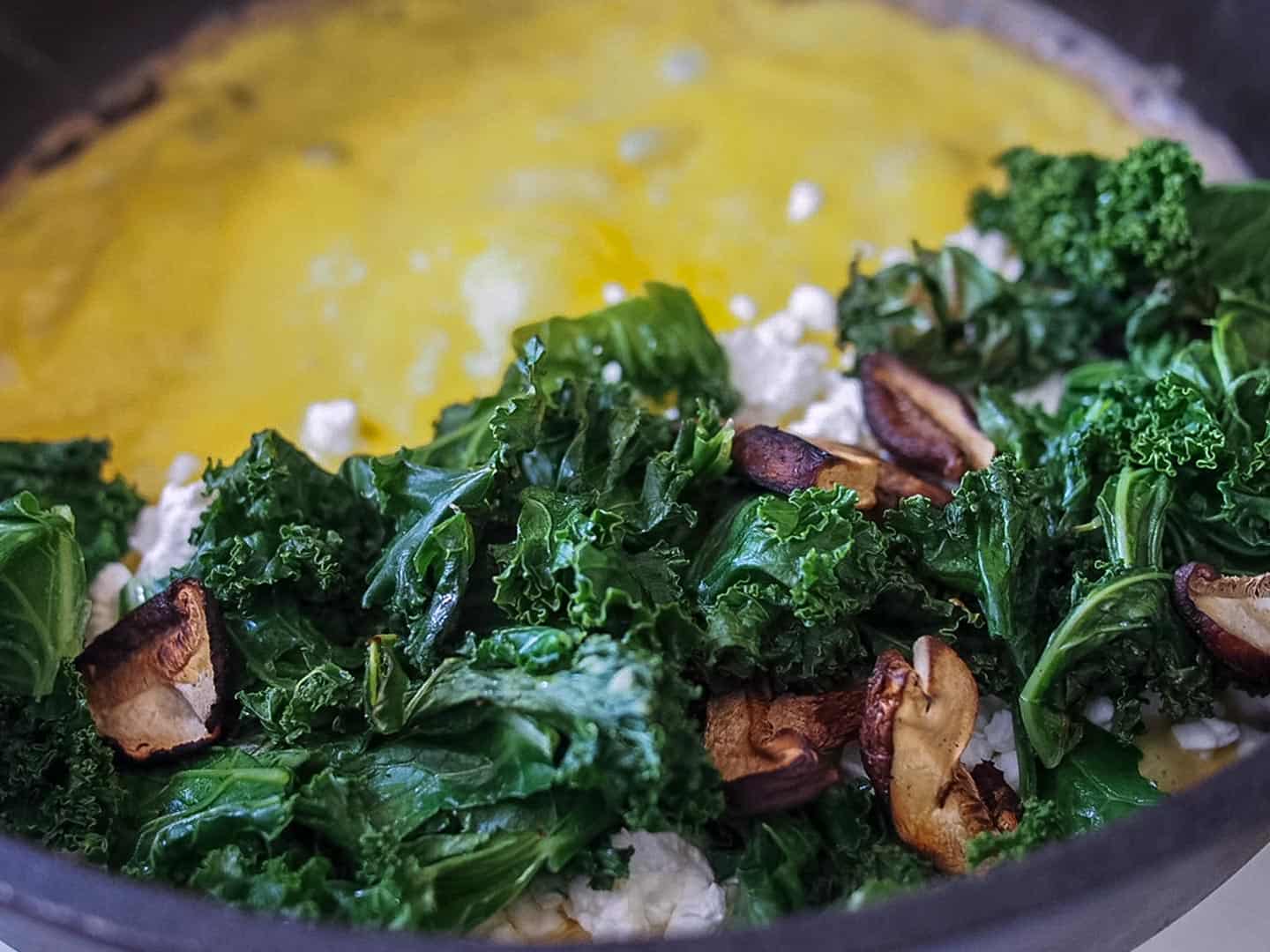 Kale mushrooms and dry cottage cheese curds on omelette in pan