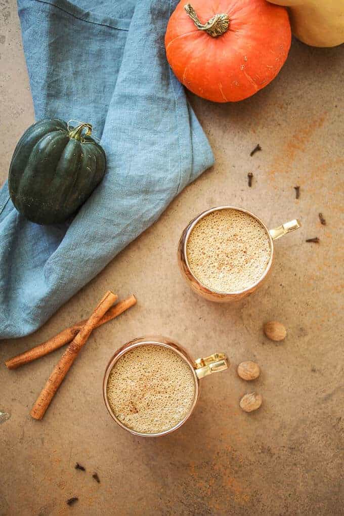 Flat lay photo of pumpkin spiced coffee in copper mugs with blue linen