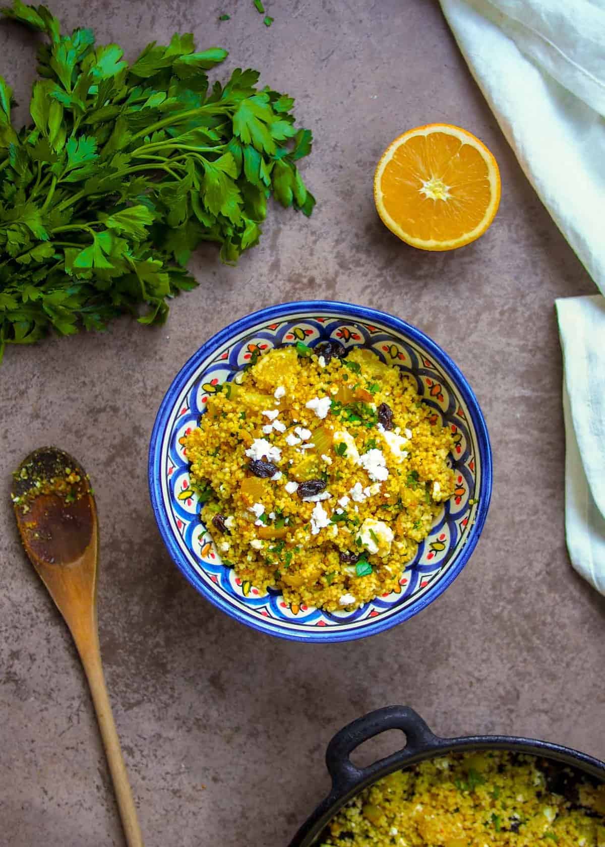 Moroccan couscous in blue bowl with wooden spoon on side and parsley