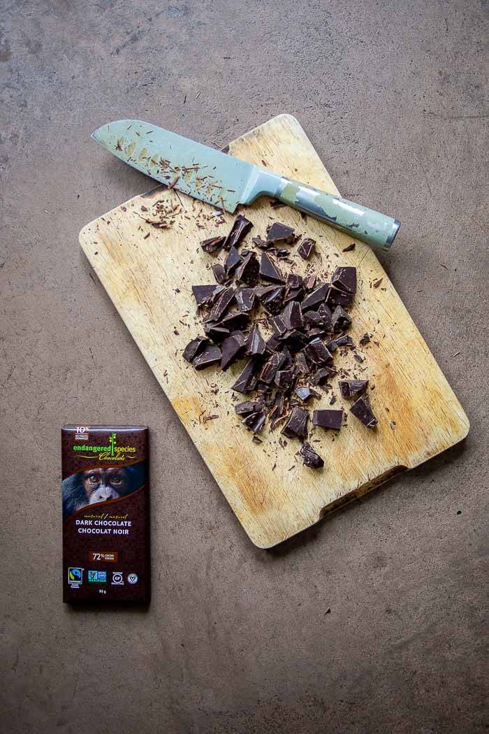 Block of dark chocolate cut up into chocolate chips and cutting board with knife