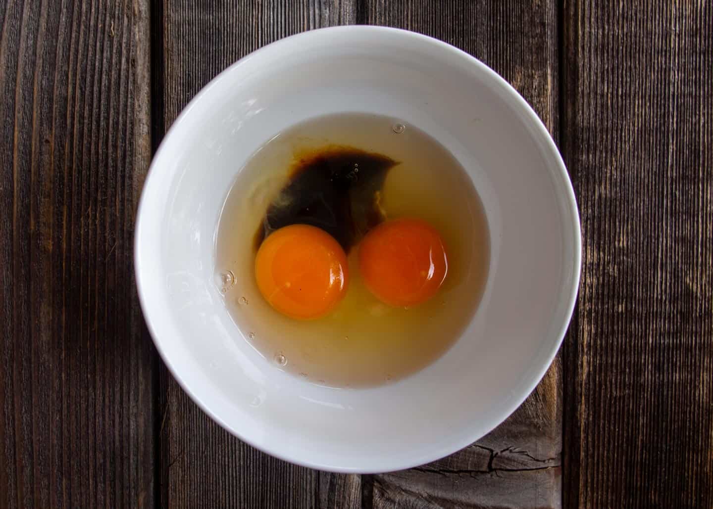 Two eggs in white bowl with soy sauce